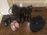 Wide view of all footwear grouped on a wood floor including ladies shoes, men's shoes, slippers, handbag, and tote bag