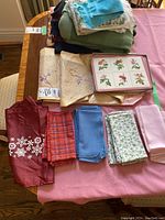 Overview of various folded table linens including runners, covers, and napkins layered on a wooden table with a pink fabric beneath.
