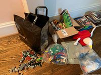 Overall view showing black bag, cardboard box of toys, clear bag with Lego pieces, and small die cast cars on the floor