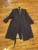 Front view of the black ladies trench coat showing buttons, epaulettes, collar, and hanging belt.