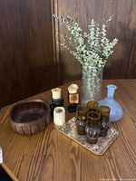 Wide view of lot: glass vases, faux branches, amber glasses in metal holder on tray, blue vase, candles, candlesticks, wooden bowl on wood table