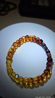 Photo of a stretchy bracelet made of rounded natural amber beads showcasing a color gradient from yellow to dark brown.