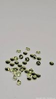 Overhead photo showing a scattered lot of small apple green peridot gemstones, round cut with faceted diamond cuts.