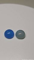 Two smooth round cabochon chalcedony gemstones, one icey blue and one arctic blue, displayed on a white background.