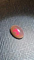 Photo of a natural black chocolate fire opal in oval cabochon form showing vivid red and orange fire hues on a black-brown matrix background.