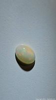 Oval cabochon natural untreated Ethiopian white opal with soft multicolored flash visible on a plain background, under natural light
