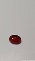 Photograph of 1.53ct oval cabochon fire orange carnelian gemstone on a plain background showing smooth polished surface and rich translucent orange-red color.