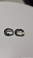 Pair of oval cut natural green amethyst (prasiolite) gemstones on white background showing faceting and color.