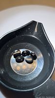 Five jet black oval cabochon gemstones displayed in a black container, showing reflective surfaces and polished finish.