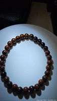 Photo showing a circular stretchy bracelet composed of polished round mahogany jasper beads with brown and black natural patterns.