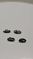 Four marquis cut natural sapphires laid out on a flat surface showing their deep green-yellow multicolor hues and faceting details.