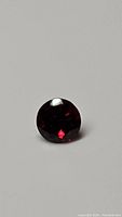 Close-up photo of the round cut cherry red garnet gemstone on a gray background.