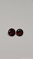 Pair of round deep red Mozambique garnet gemstones on a plain white background.