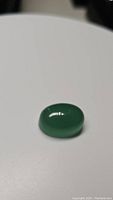 Oval polished natural green aventurine cabochon gemstone against white background, showing the smooth surface and natural green color.