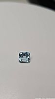 Close-up photo of a square step cut natural lagoon blue aquamarine gemstone on a neutral background.