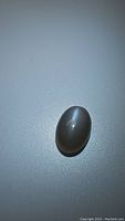 Oval cabochon silver moonstone on a grey background showing cat's eye effect and flash