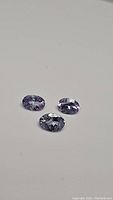Three oval cut natural tanzanite gemstones on white background showing light blue to purple color and some inclusions.