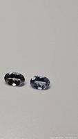 Pair of natural oval cut tanzanite gemstones viewed slightly from the top on a neutral background.