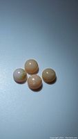 Four small round cabochon pink opal stones lying flat on a white surface with visible inclusions and variations in color, close-up image.
