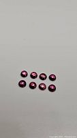 Photo showing eight round cabochon raspberry pink sapphires arranged in two rows on a white surface.