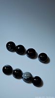 Six round polished snowflake obsidian cabochons loosely grouped on a white surface. Black color with white snowflake patterns visible on each stone.