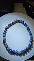 Top-down photo of the natural blue sodalite bracelet displayed on a white circular stand showing the full bracelet with its varying blue and gray beads.