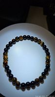 Photo of a tigerseye bead bracelet laid flat in circular shape on white plate, showing the color and pattern of each bead.