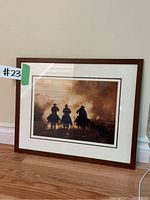 Framed art print titled "Dusty Riders" by Betty Andres resting against a wall on wooden floor, showing entire piece with matting and frame.