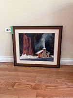 Full view of the framed photographic artwork depicting a cabin in a winter forest scene with smoke rising from the chimney, against a backdrop of large trees.