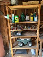 Wooden shelving unit holding multiple gardening supplies and tools. Contains bottles, tools, plastic garden wagon, wire and trays.