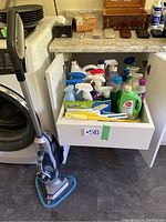 View of Hoover SteamVac floor cleaner and drawer open exposing various cleaning sprays, sponges and tools inside.
