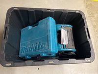 Black plastic storage bin containing teal Makita items