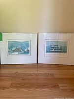 Pair of framed village and church art prints against a blank wall, showing full views of both artworks.