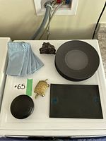 Overview photo showing six black dinner plates stacked, six light blue cloth napkins folded, two brass turtle figurines, one ornate black metal trivet on a white surface.