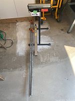Full view of roller slide stand and two bar clamps on concrete floor in garage.