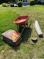 Wide view of wheelbarrow, mulch bags, garden tools, and landscaping fabric on lawn