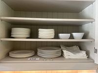 Cabinet shelf with stacks of small round plates, square plates and two medium bowls.