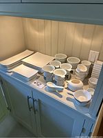 Wide view of dishware including mugs, medium bowls, small scalloped bowls, ceramic spoons, and various size plates.