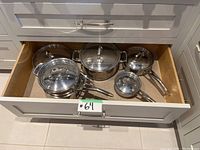 Five-piece cookware set arranged in kitchen drawer, showing all pots, pan, insert and lids.