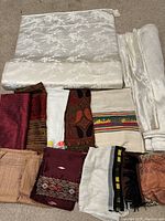 Top view showing assortment of folded fabrics including two large cream silk bolts with floral brocade and multiple smaller colorful patterned fabrics.