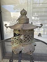 Front view of the antique Japanese pagoda lantern showing door slightly ajar and the metal latticework, as well as small hanging bell on the right side.