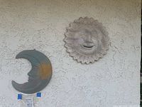 Photo of both ceramic sun and moon wall hangings on a beige stucco wall, showing full details of both items.