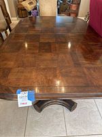 Top view of wooden dining table surface with wood grain and rounded corners, showing label with measurements and lot number.
