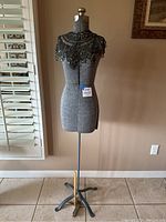 Full view of gray fabric-covered vintage dressmaker mannequin on adjustable metal stand with four legs and black lace hand beaded Victorian collar capelet draped over shoulders.