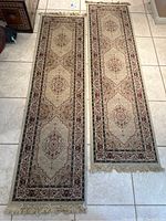 Two traditional cream and burgundy Turkish style runner rugs laid flat on tile floor, showing full length and pattern details with fringed ends visible.