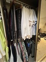 Closet rack of men's dress shirts in white and light colors with dress slacks below