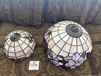 Pair of two Tiffany-style stained glass lamp shades, one smaller and one larger, placed on patterned fabric.