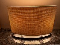 Front view of the oval lamp showing woven textured shade and metallic base on a dark marble surface.