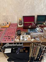 Overview of table showing multiple pink velvet-lined trays holding rings, earrings and small jewelry, wooden boxes and display pieces in background