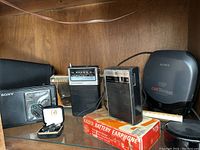 Overview of Sony Walkman cassette player, carrying case, Concord earphone kit, Lloyd's and GE radios on red Radio Battery Earphone box, and Sony ESP Car Discman